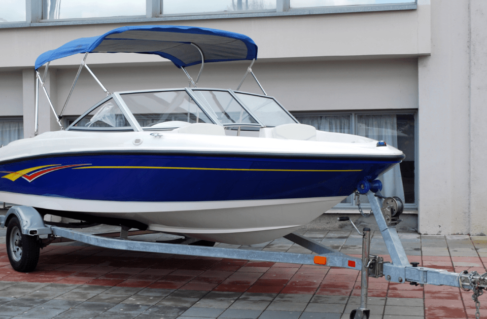 Blue and white motorboat on a trailer, parked in front of a building.