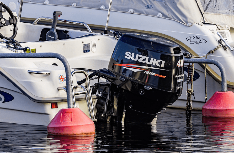 Suzuki 40 outboard motor mounted on a white boat near red buoys in water.