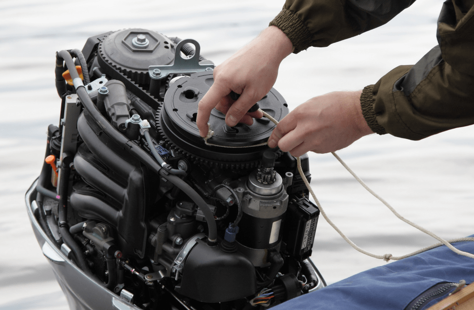 Person repairing an outboard motor, with hands working on engine parts.