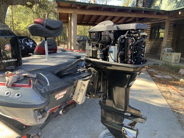 Bass boat with a black outboard motor, outdoors on a concrete surface. Engine exposed for maintenance.