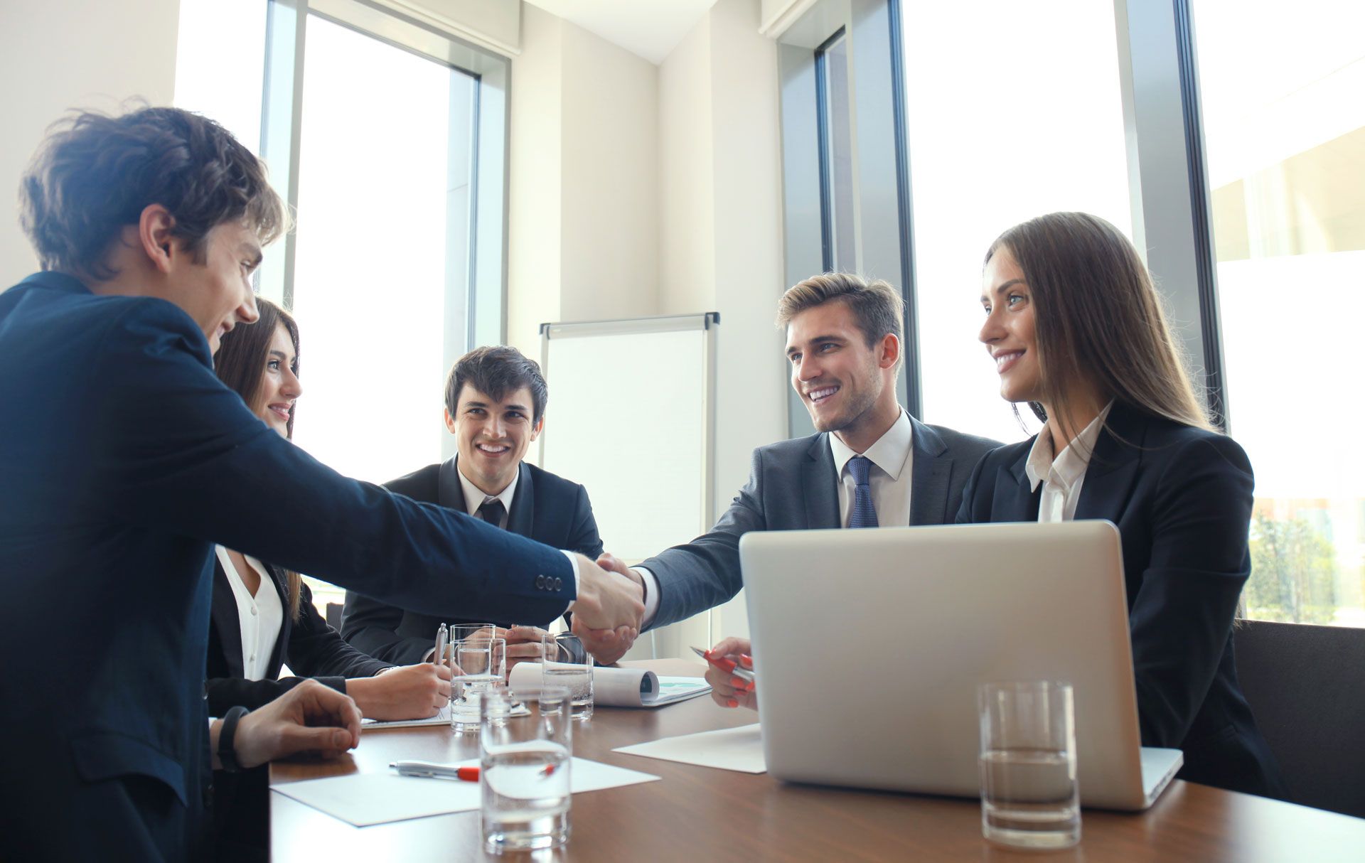 Business people shaking hands at a table in an office, smiling.