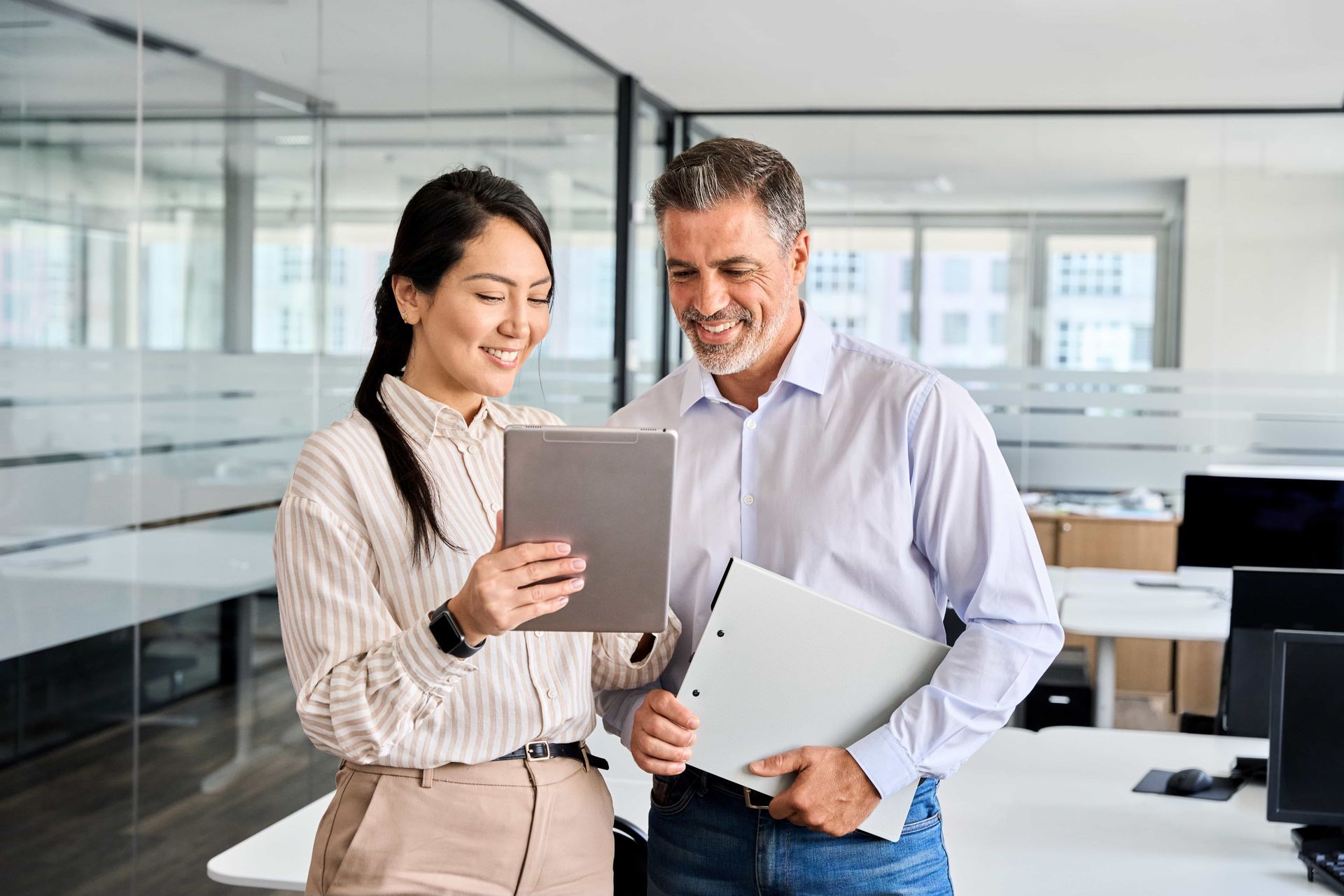 A man and a woman are looking at a tablet in an office.