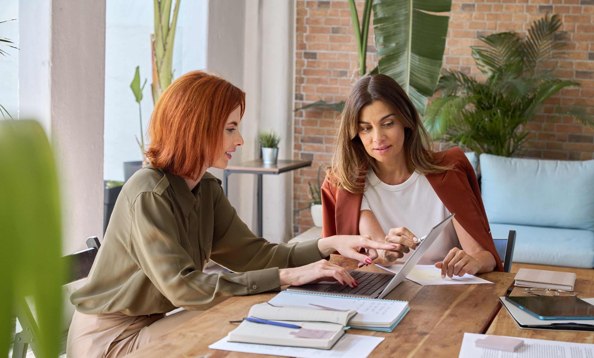 Two women are sitting at a table looking at a laptop.