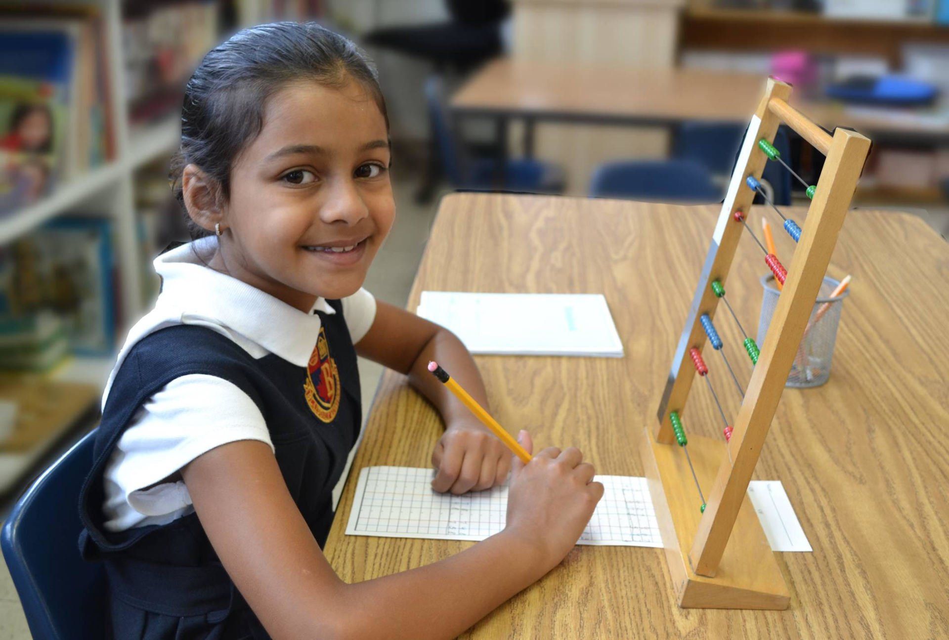 A young girl is sitting at a desk using an abacus