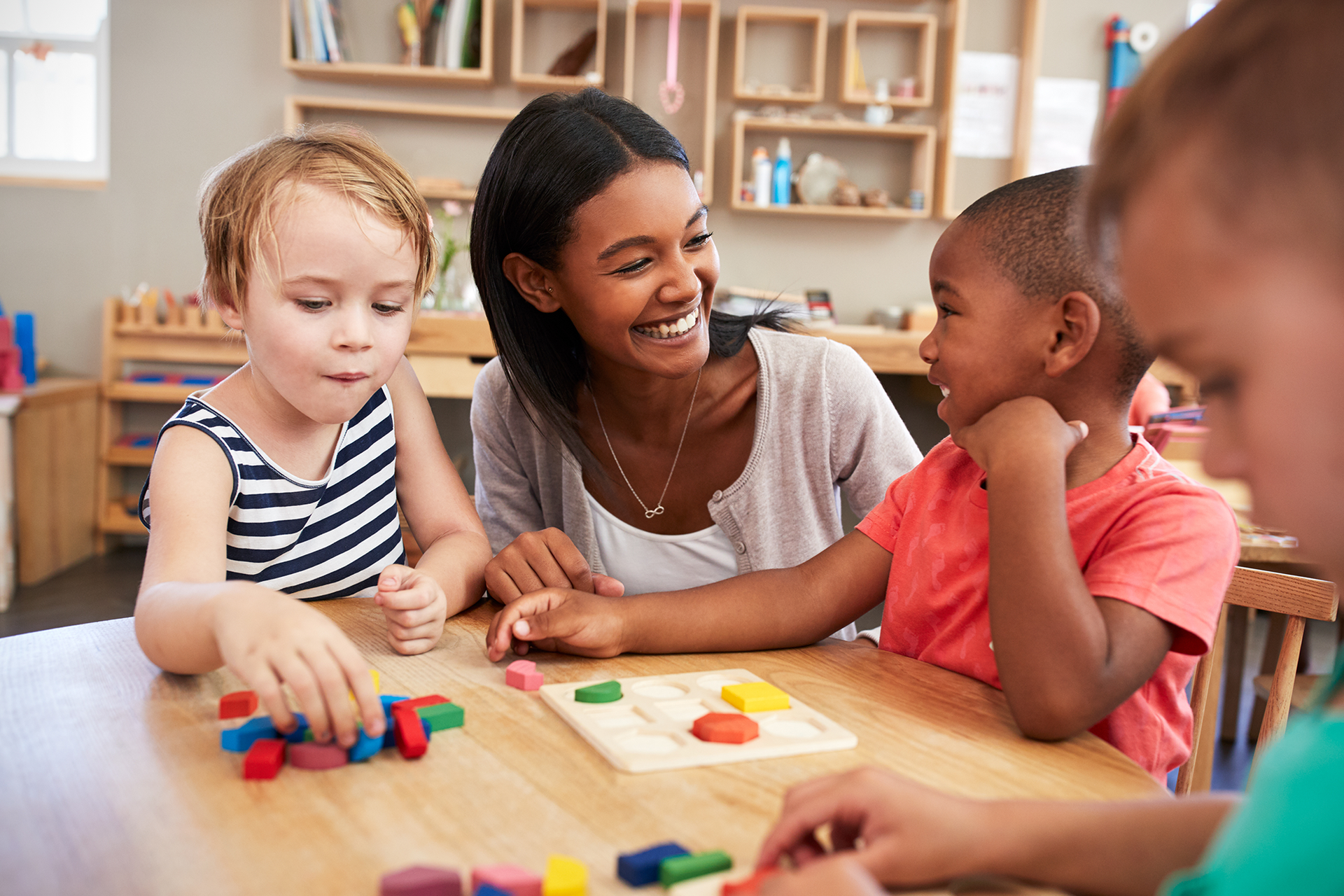 A teacher is playing with children at a table in a classroom.