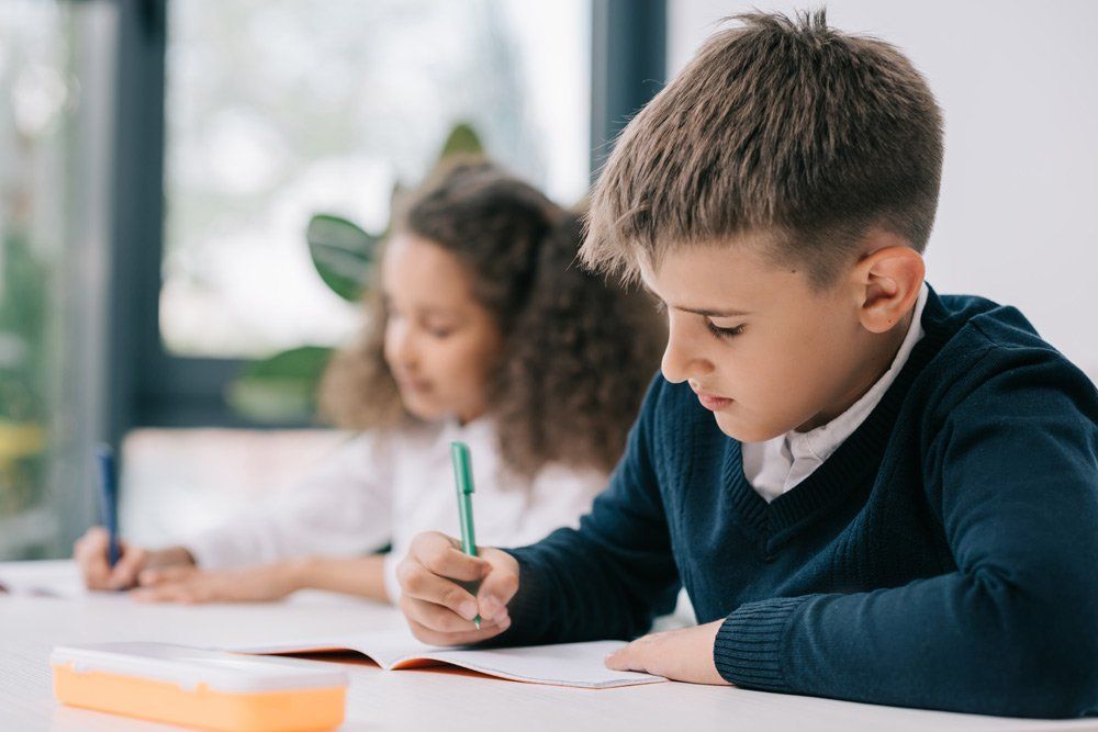 A boy and a girl are sitting at a table writing in a notebook.