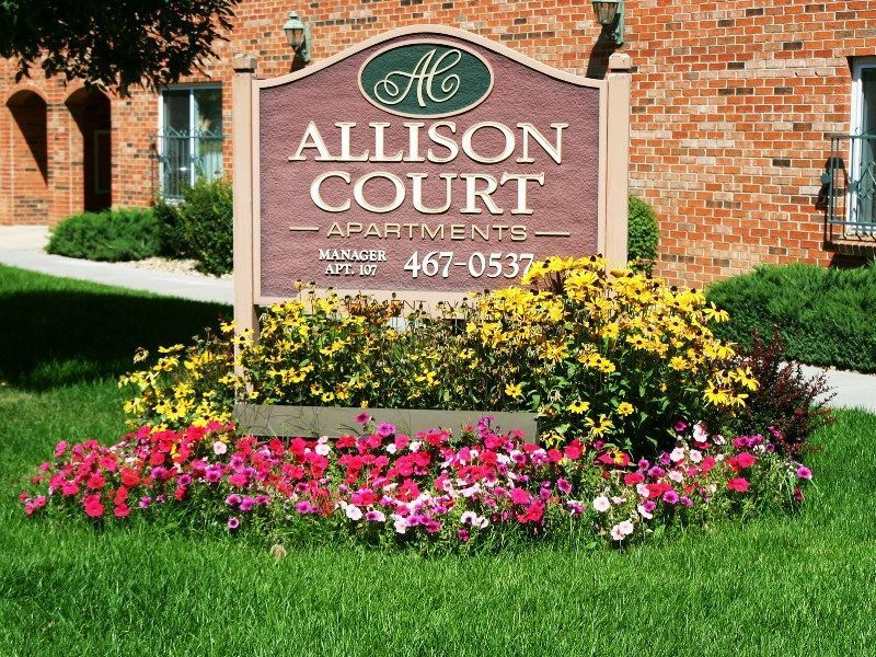 A sign for allison court apartments is in front of a brick building