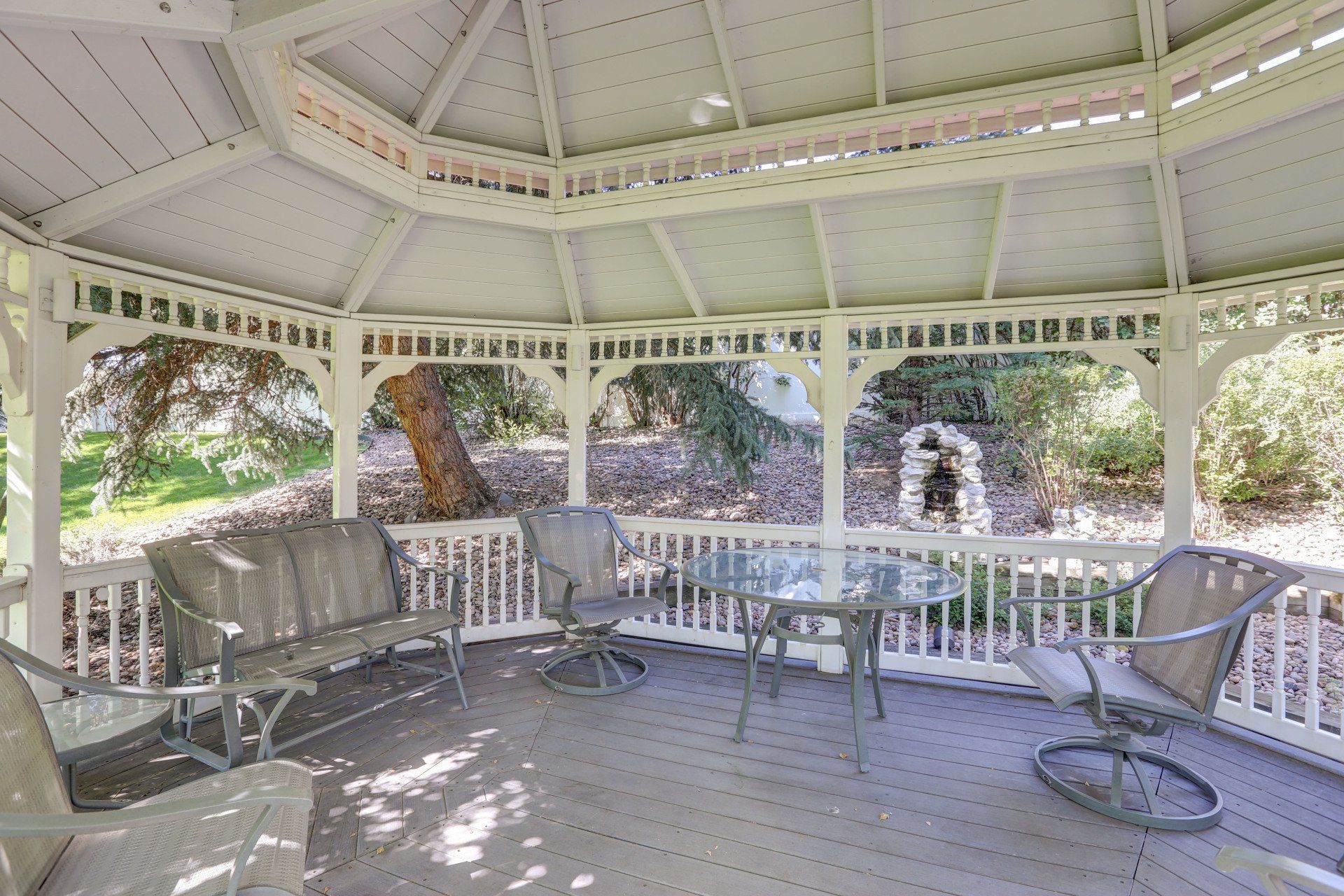 A white gazebo with a bench , chairs , and a table.