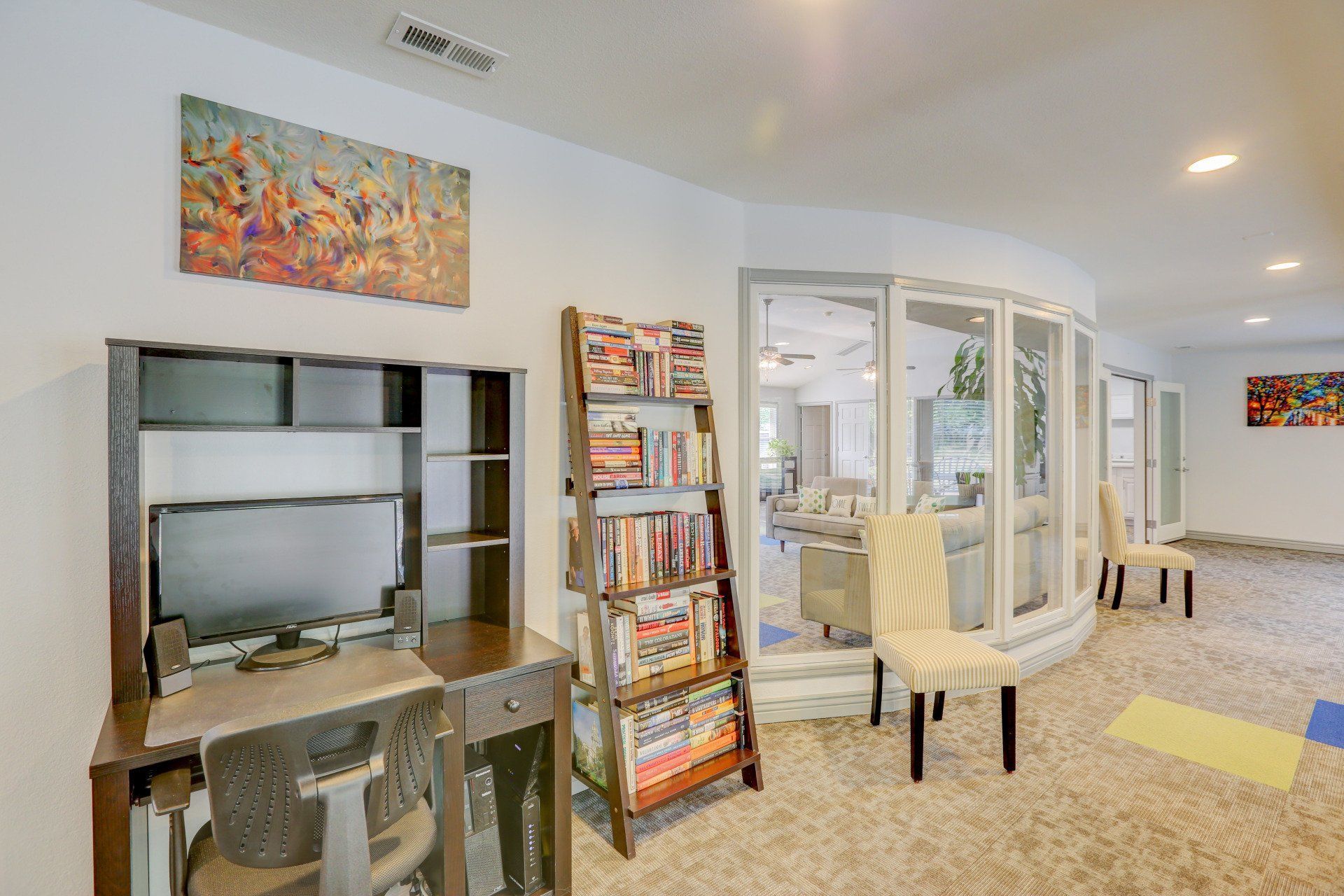 A living room with a desk , chairs and a bookshelf.