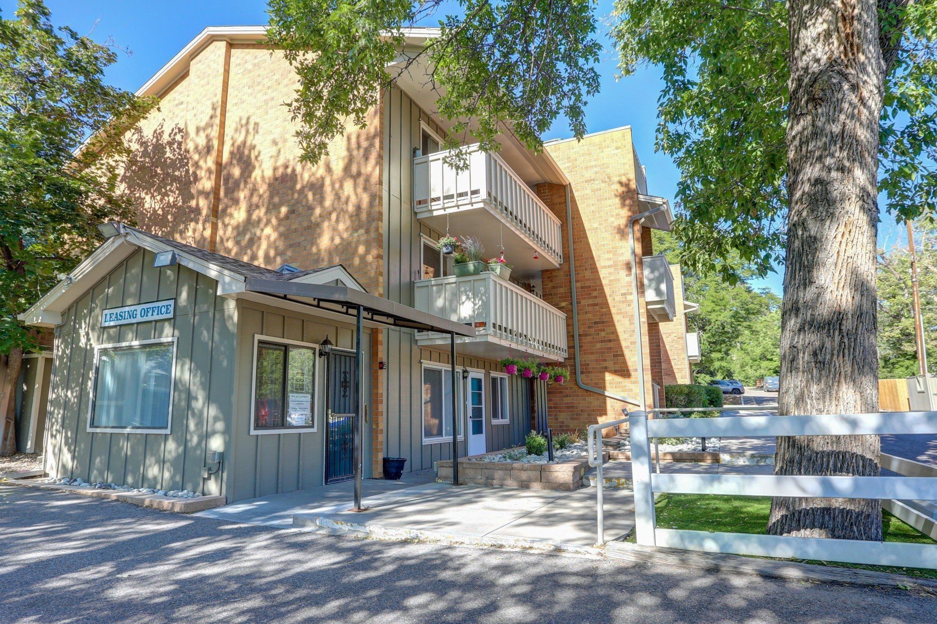 A large apartment building with a fence and trees in front of it.