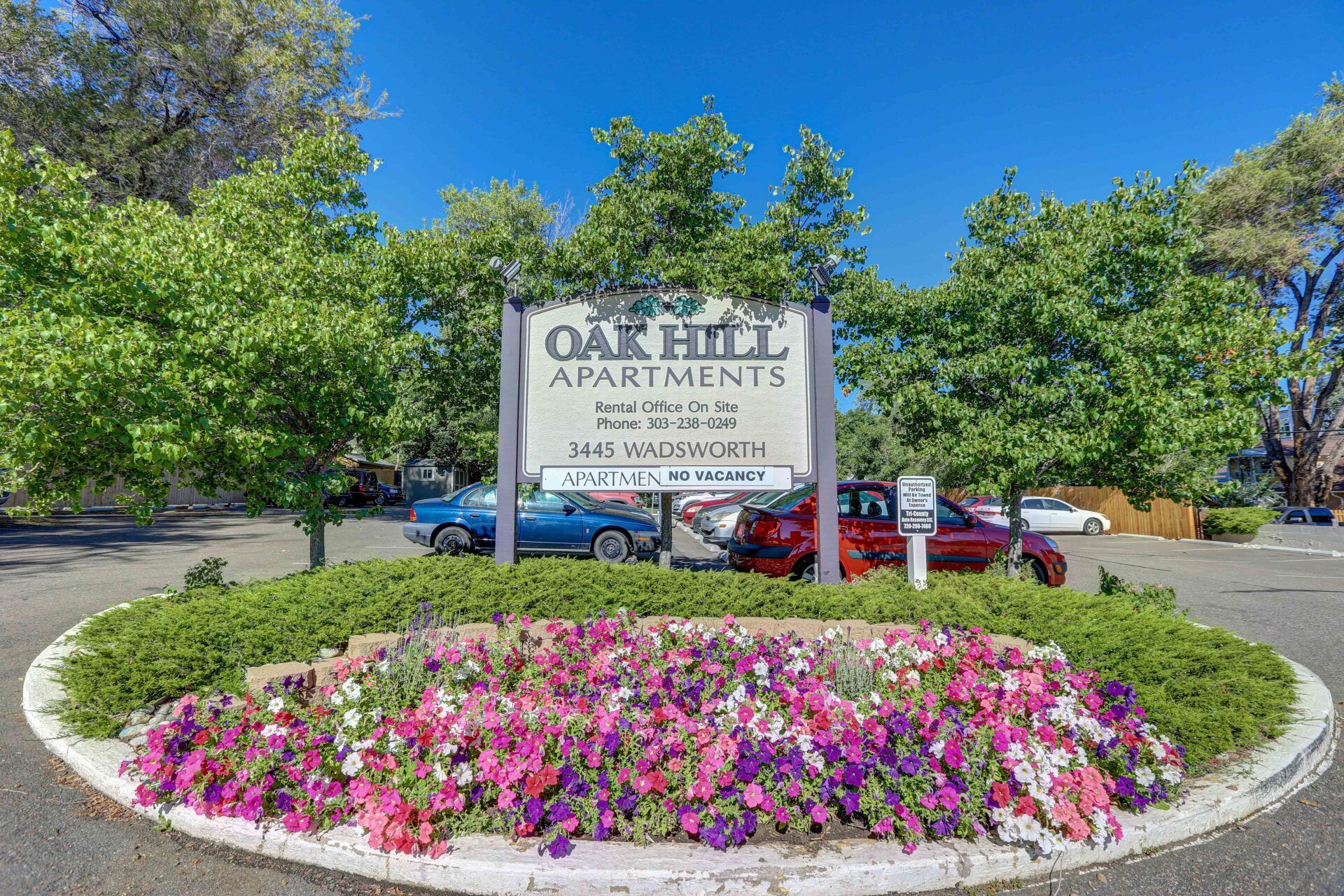 A sign for oak hill apartment is surrounded by flowers and trees.