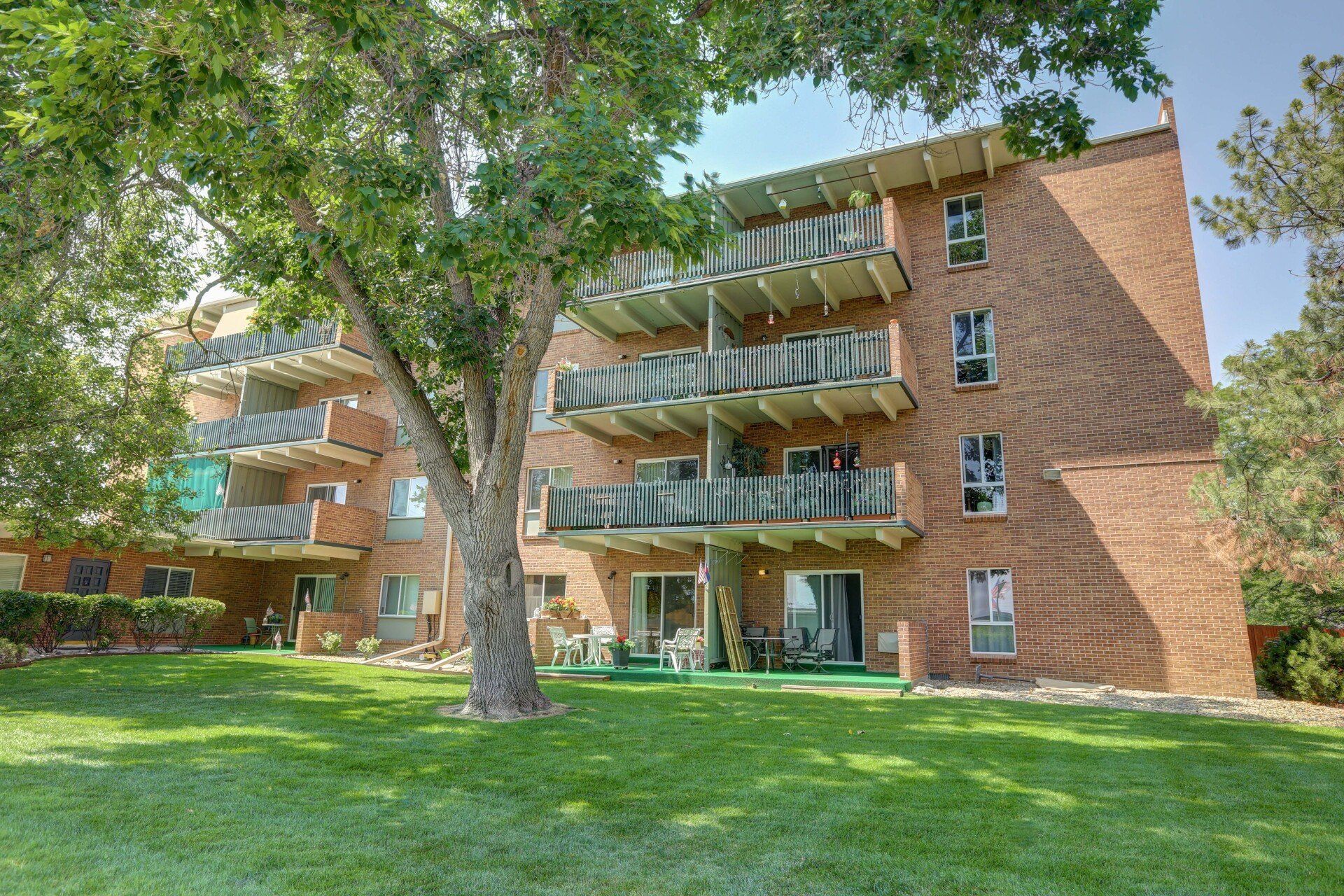 A large brick apartment building with lots of balconies and a tree in front of it.