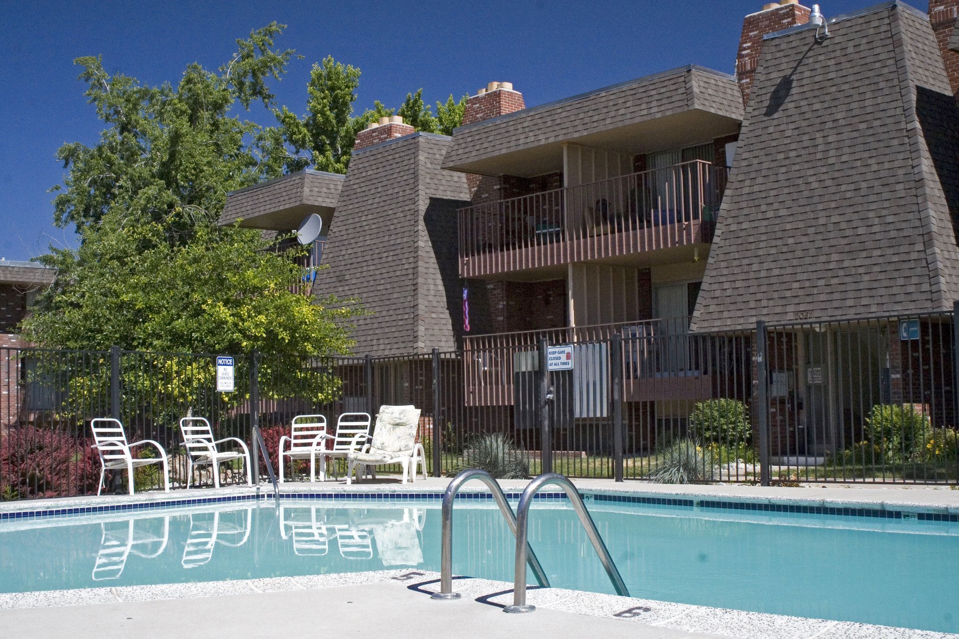 A swimming pool in front of a building with chairs around it
