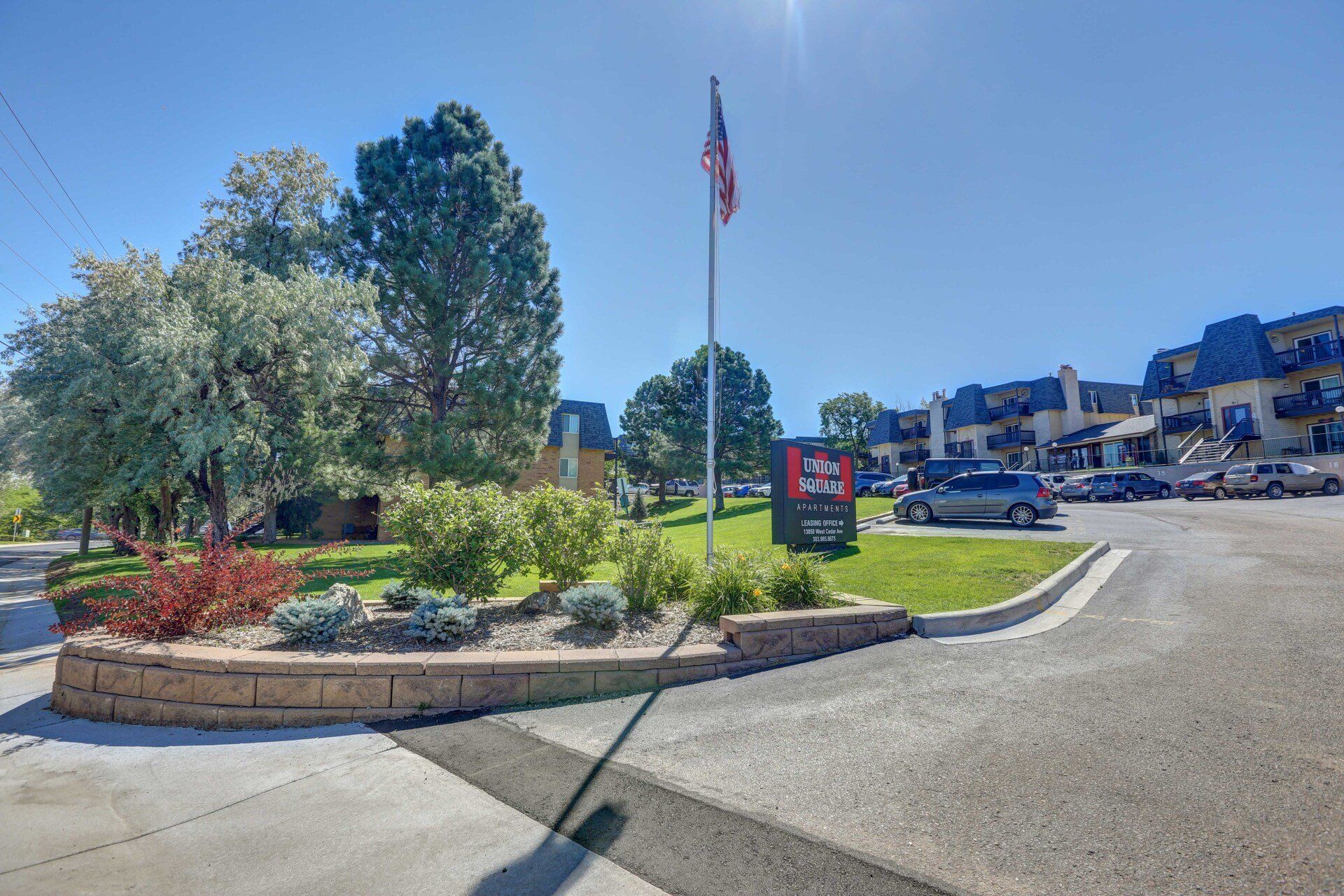 A parking lot with cars parked in front of a building with a flag on a pole.