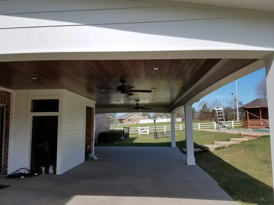 A covered patio with a wooden ceiling and a ceiling fan.