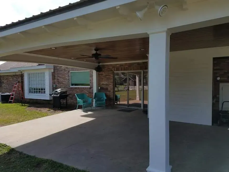 A covered patio with chairs , a grill and a ceiling fan.