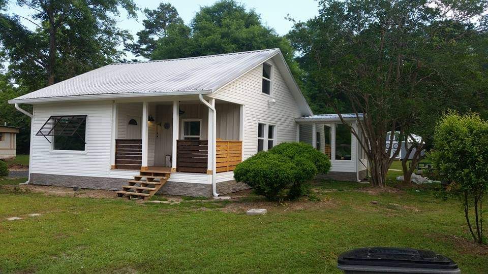 A small white house with a porch is surrounded by trees and grass.