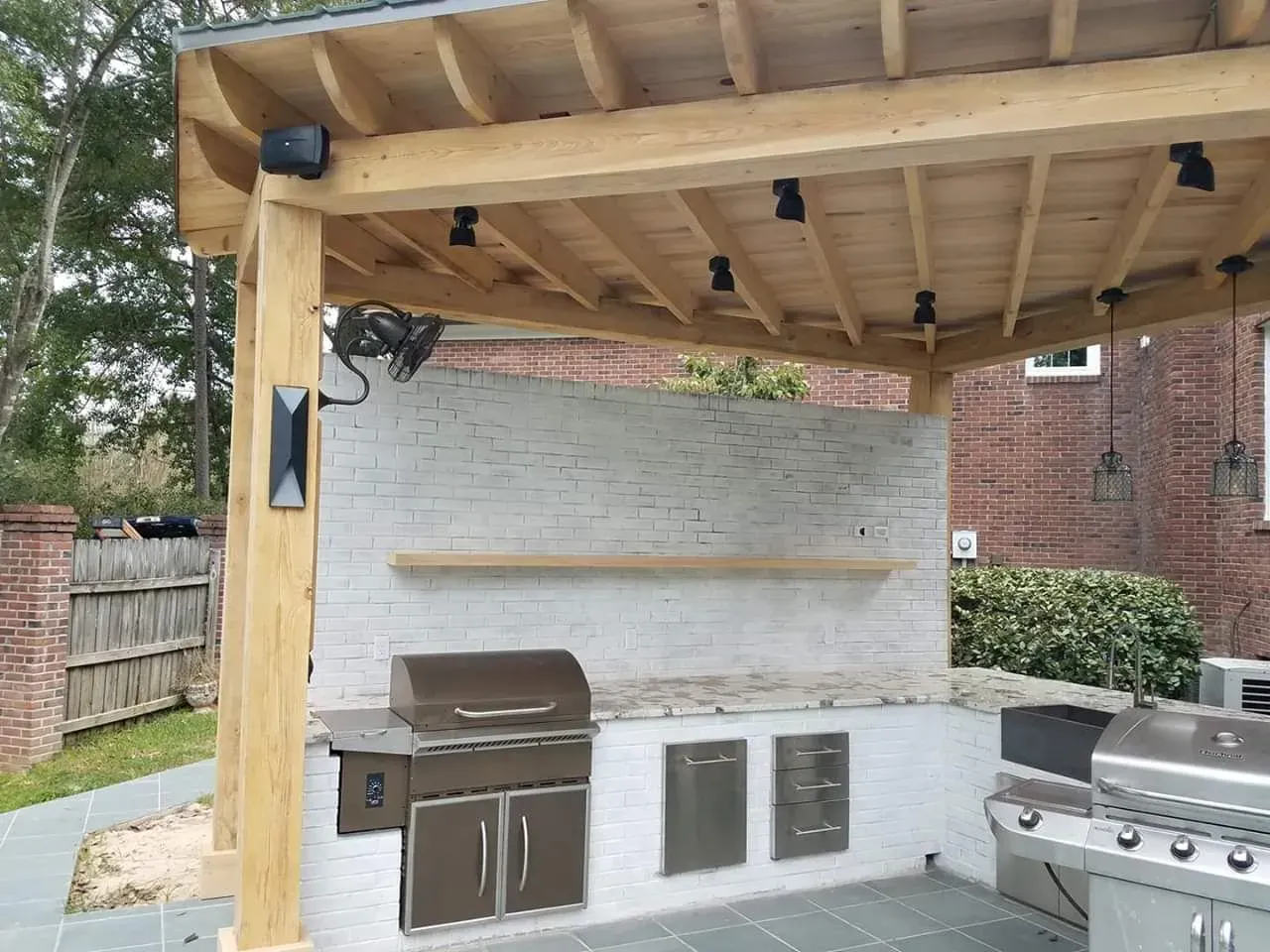 An outdoor kitchen with a grill under a wooden pergola.