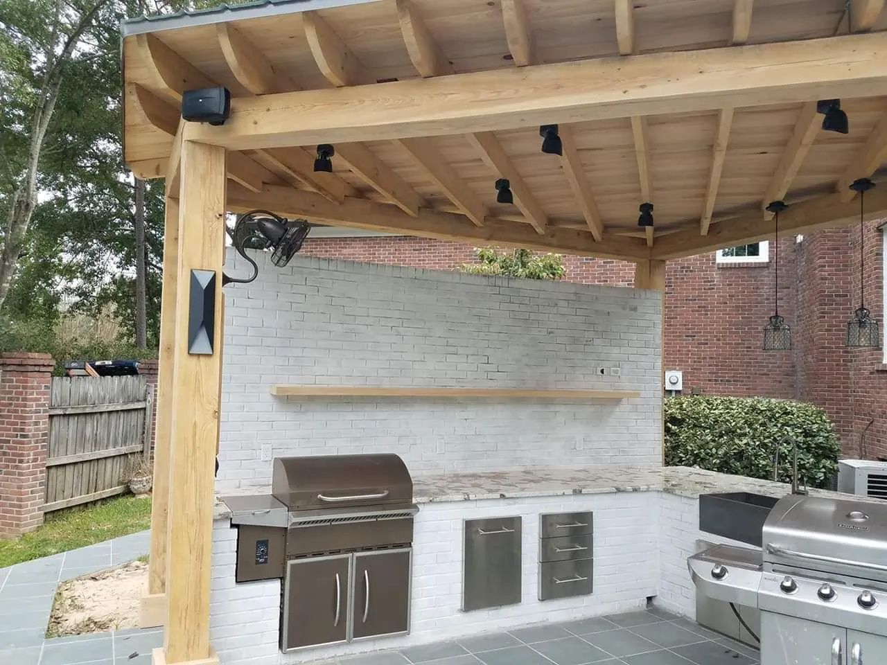 An outdoor kitchen with a grill under a wooden pergola.