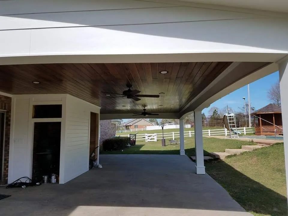 A covered porch with a ceiling fan and a fence in the background.