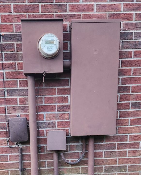 A brick wall with a meter and a box attached to it.