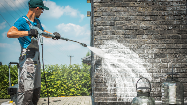 Man power washing a brick wall. Outdoors, bright sun.