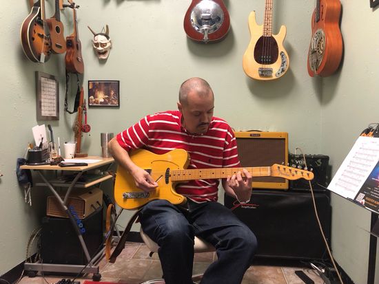 David Dunavant is teaching guitar lessons in a room with many guitars on the wall, located in little rock Arkansas.
