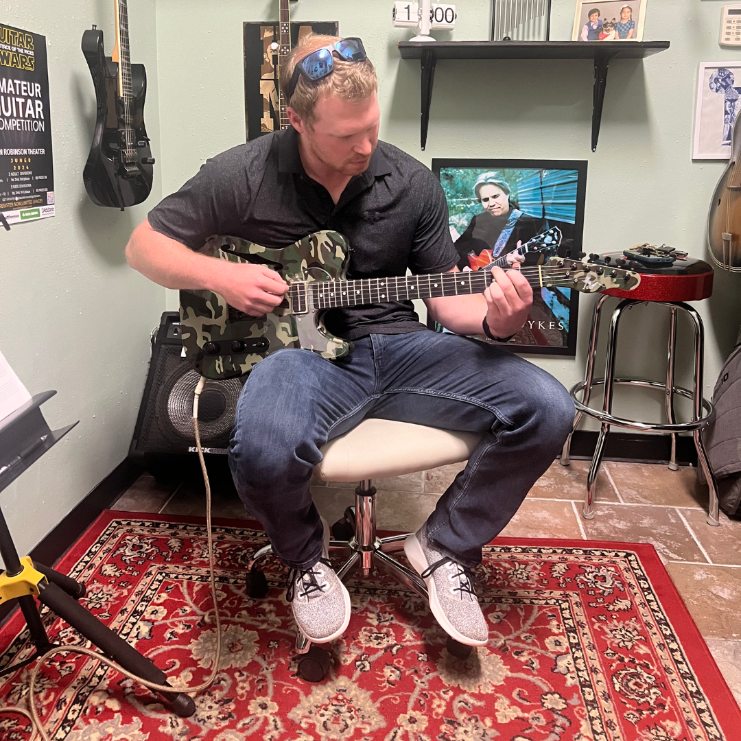 A man is sitting in a chair playing a guitar with David Dunavant while getting guitar lessons in Little Rock, AR