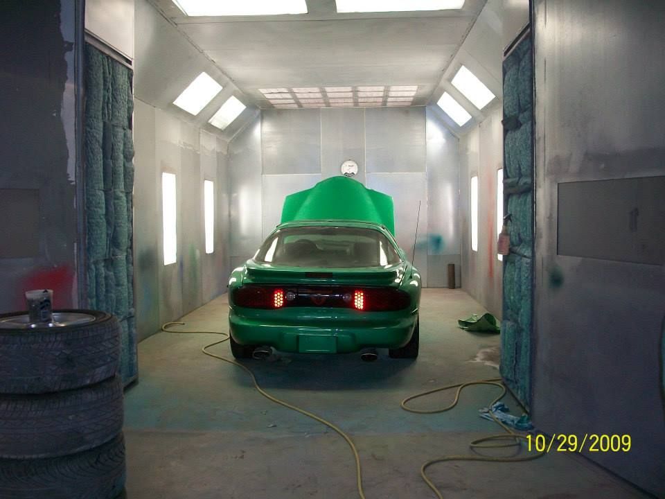 Green car in a paint booth with bright lights and masking paper covering it