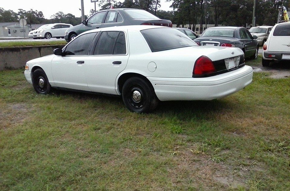White sedan parked on grass in a lot, with other cars in the background.