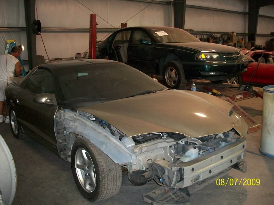 Two cars in a garage; foreground silver car has damaged front left bodywork.
