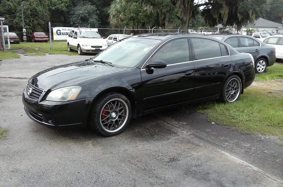 Black sedan parked on grass beside a road, with another car in the background.