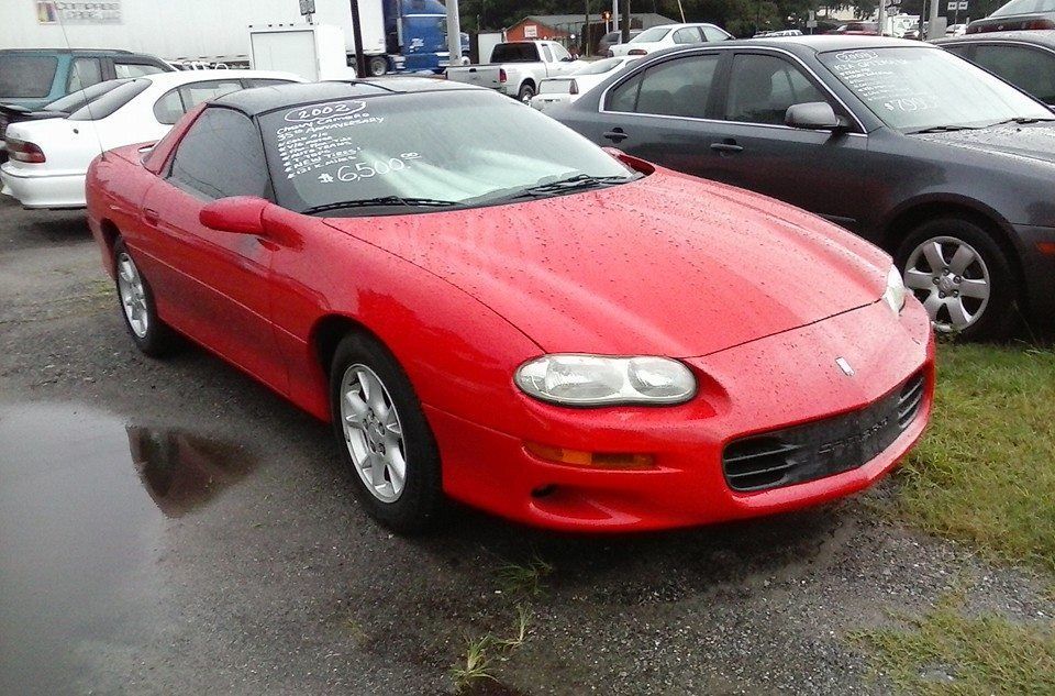 Red sports coupe parked on a wet lot, with other cars in the background.