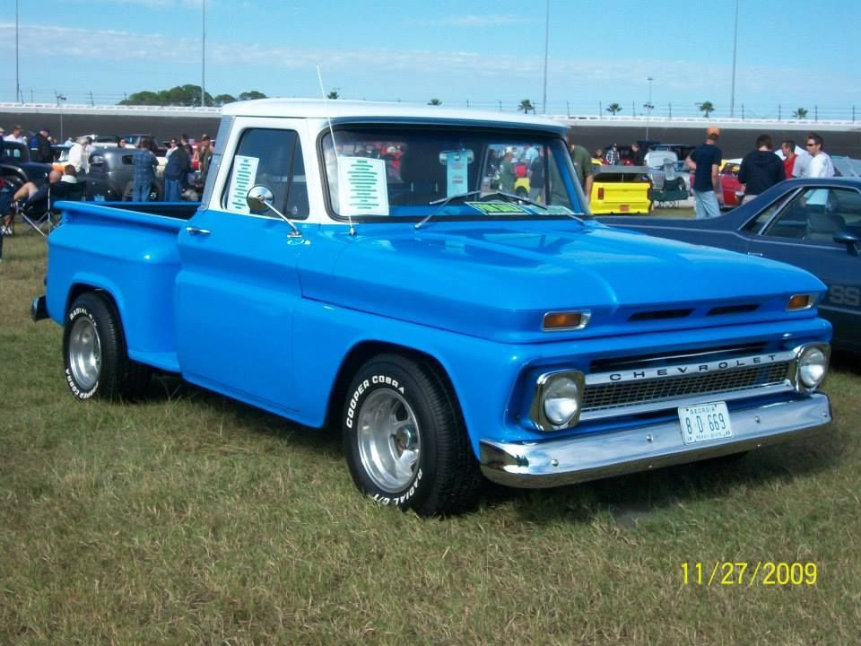Bright blue vintage pickup truck parked on grass at an outdoor car show