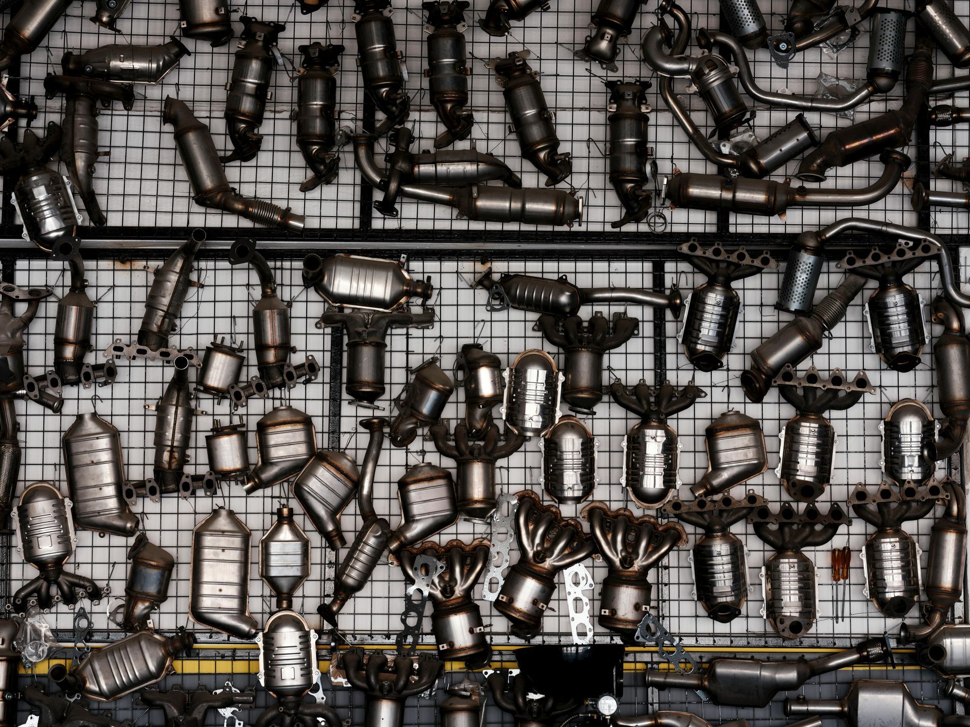 Rows of hanging black-and-silver metal pipes and fittings on a wire grid wall.