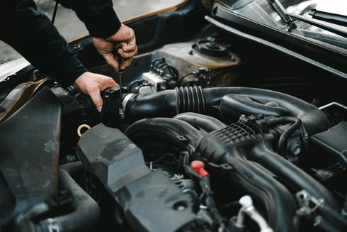 Mechanic inspecting a car engine with hands near hoses and components under the hood