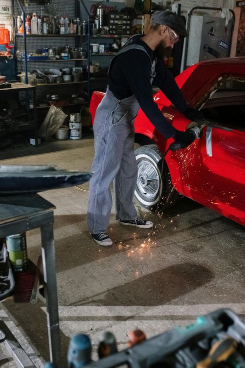 Person welding a red car in a cluttered garage, with sparks on the floor.
