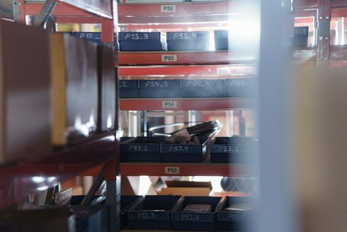 Stacked red warehouse shelves with black bins and stored items in a storage aisle