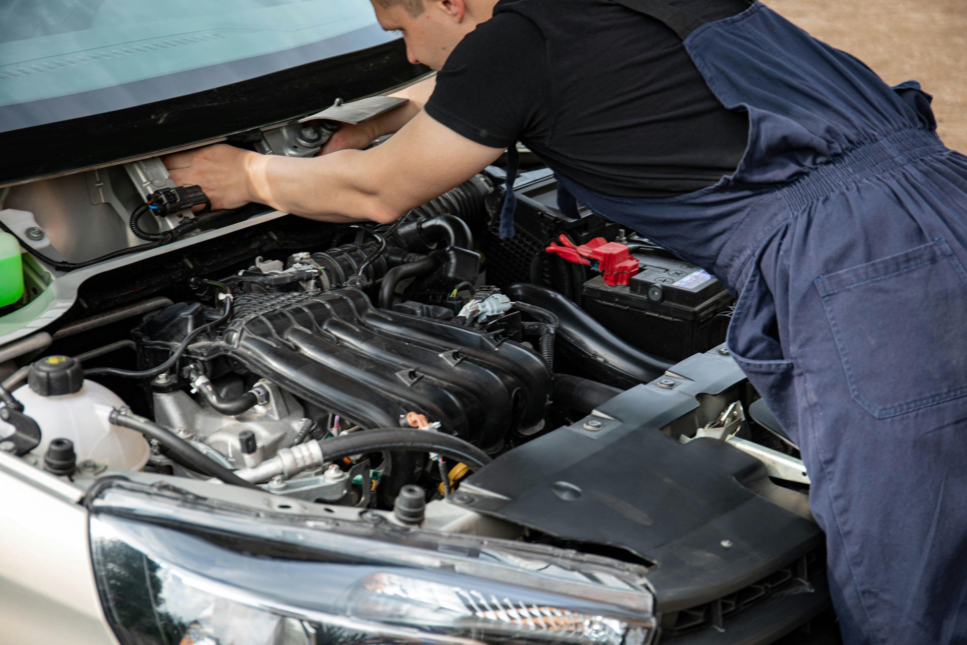 Mechanic in blue overalls working under a car hood in a garage