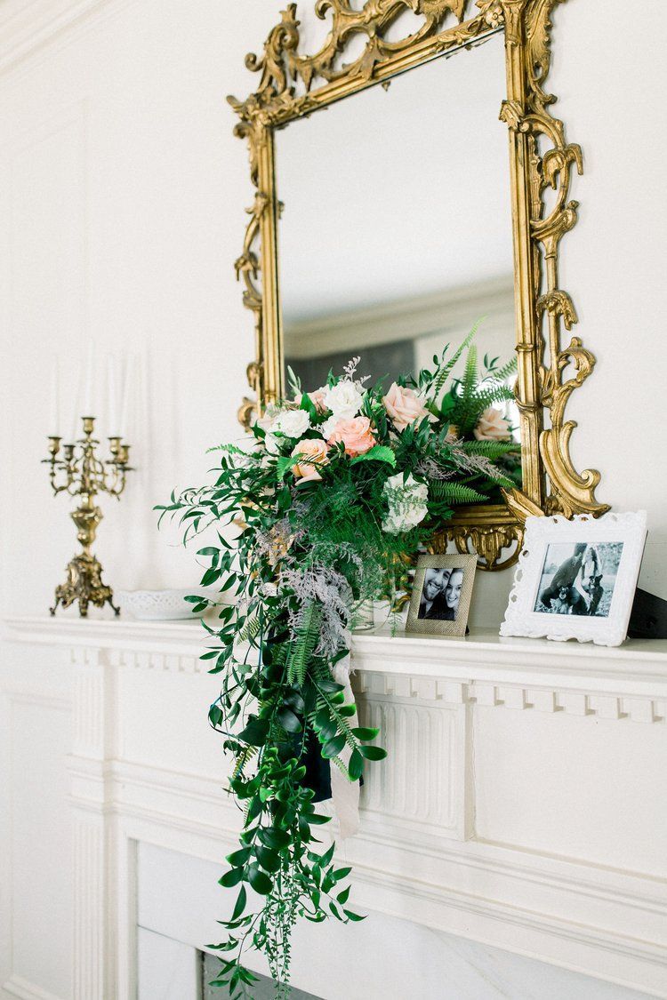 A mantle with flowers and a mirror on it.