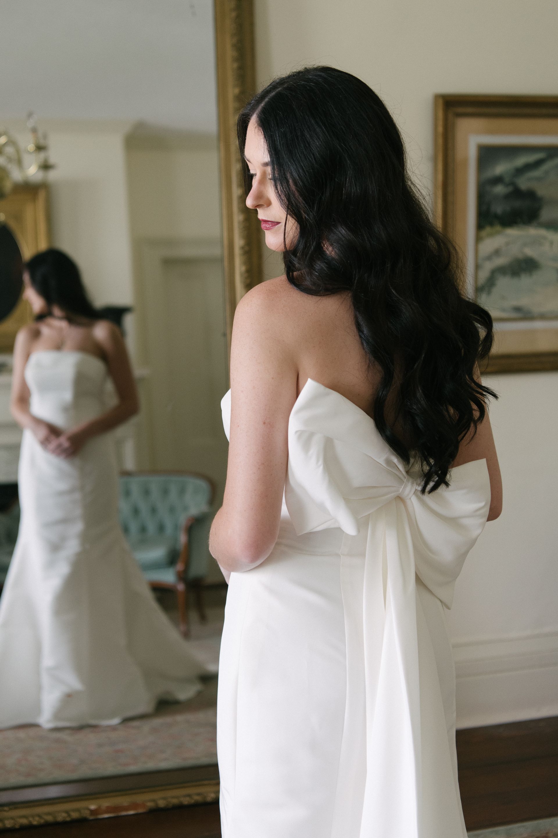 A bride in a wedding dress is standing in front of a window.