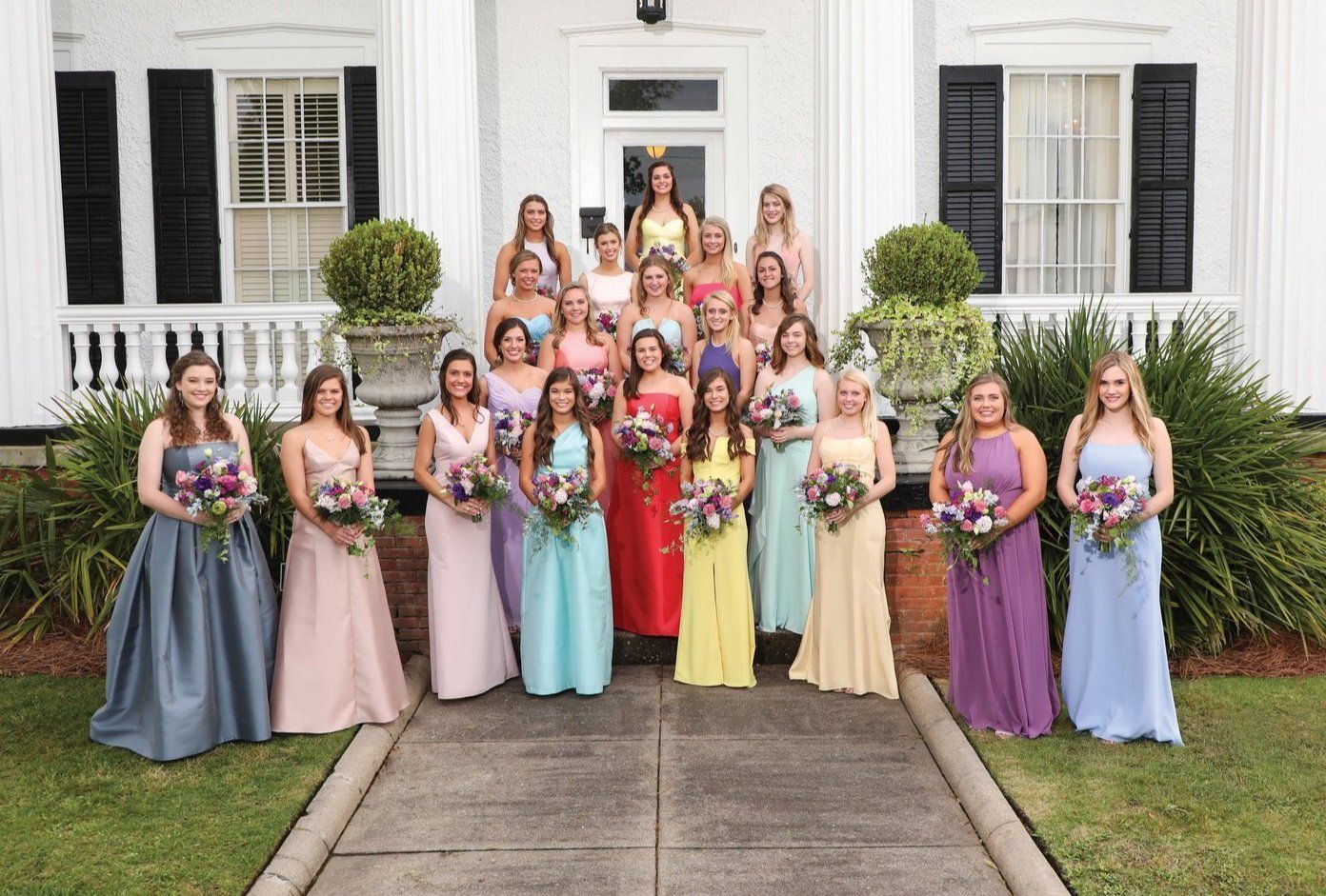 A group of women in dresses are posing for a picture in front of a house.