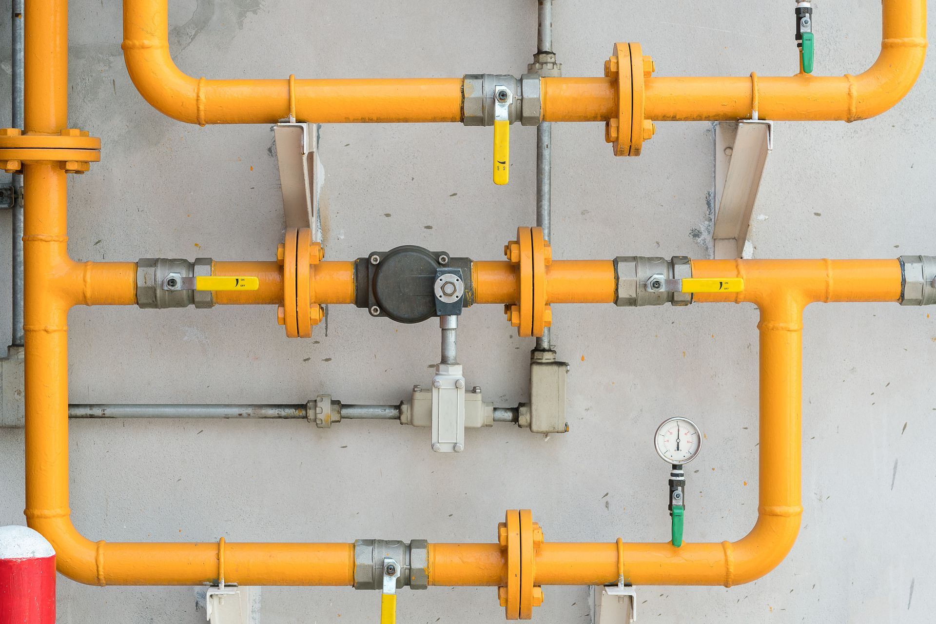 Orange gas pipes and valves mounted on a white wall with pressure gauges and fittings.