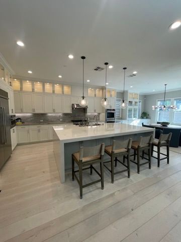 A modern, well-lit kitchen with white cabinetry, a large marble-topped island, four bar stools, and light wood flooring.