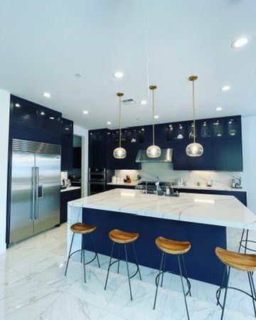 A modern kitchen featuring navy blue cabinets, a white marble island with four wooden stools, and three pendant lights.