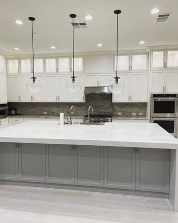 A bright, modern kitchen featuring a large white island with gray cabinets, white upper cabinets, and three globe lights.