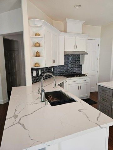 A bright kitchen featuring a white quartz island with a dark sink, white cabinetry, and a dark tile backsplash.