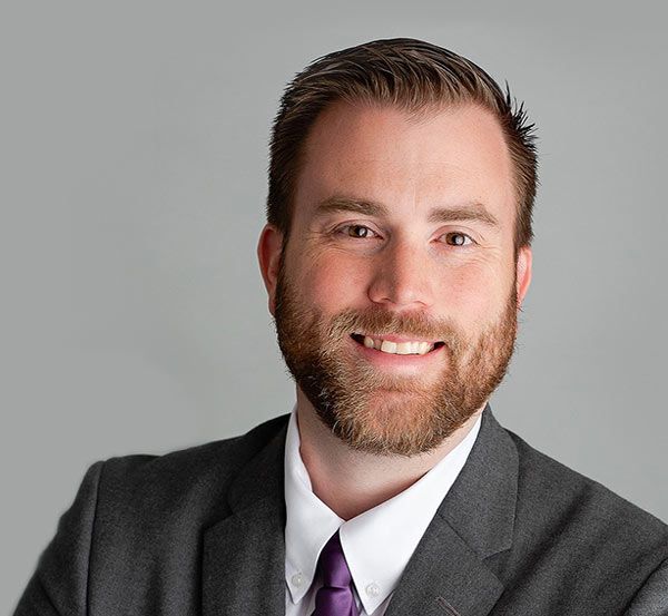 A man with a beard is wearing a suit and tie and smiling.