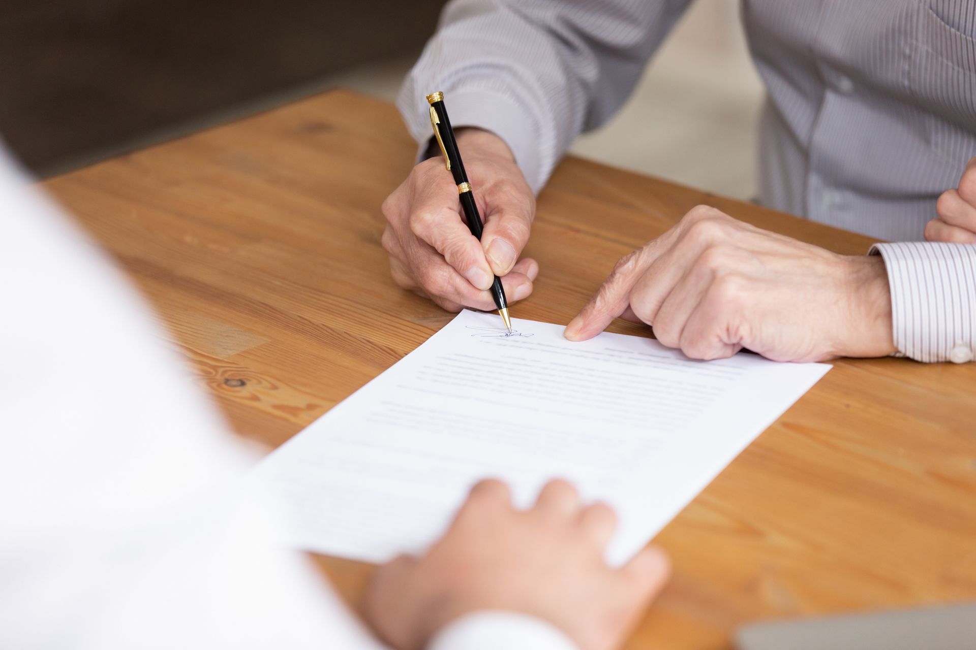 Two people are signing a document on a wooden table.
