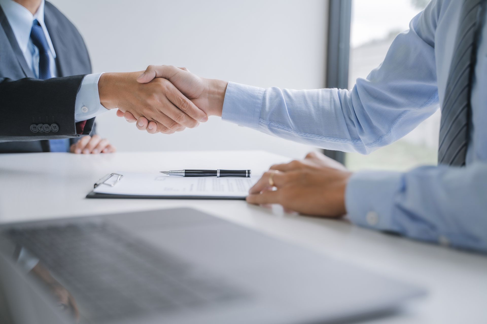 Two businessmen are shaking hands while sitting at a table.